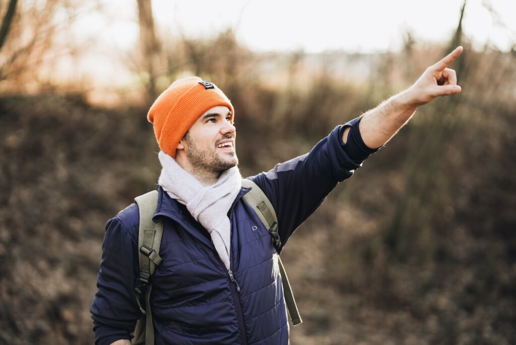man in black jacket and orange knit cap raising his right hand